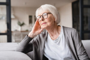 An older Caucasian woman sits on a couch looking sad or depressed.