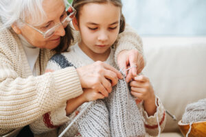 Senior woman teaches little girl how to knit wool threads with spokes. Closeup image